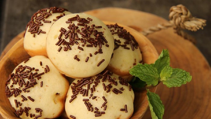 Kue Cubit, a popular street food and snack from Betawi, Jakarta. It is the Indonesian version of Dutchs poffertjes; with added topping of chocolate sprinkles instead of powder sugar. The kue cubit are arranged on a natural wooden bowl. A wooden block is used as the base; which then placed on a metal baking sheet.