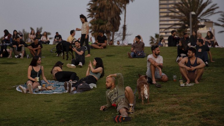 Israel Cabut Aturan Pakai Masker, Warga Bebas Hirup Udara Segar People without face masks watch the sunset, in Tel Aviv, Israel, Sunday, April 18, 2021. Israel has lifted a public mask mandate and fully reopened its education system in the latest easing of coronavirus restrictions following its mass vaccination drive. (AP Photo/Oded Balilty)
