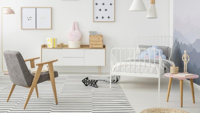 Pink table and grey wooden armchair in girls bedroom interior with mockup of empty poster