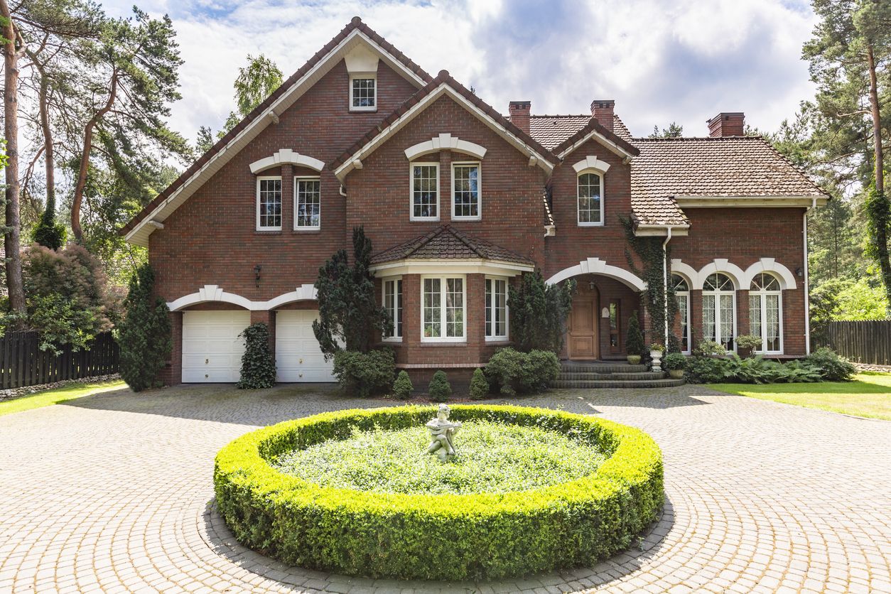 Ilustrasi Rumah Klasik Front view of a red brick English style classic house with a steep roof, large windows and a circular driveway with a flowerbed decoration in the front.