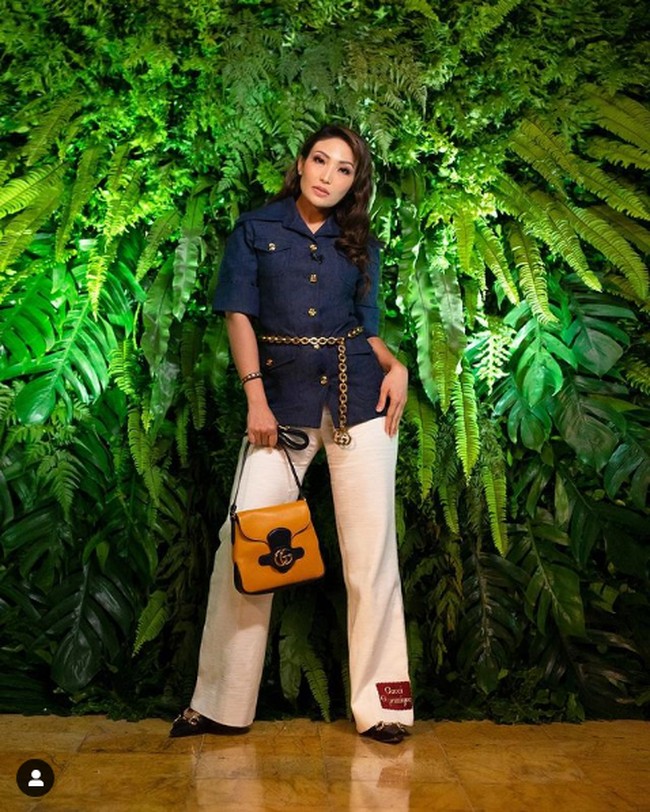 Tiga selebriti hadir untuk menonton preview show koleksi terbaru Gucci Aria. Ayu Dewi merupakan satunya. Ia tampil chic dengan kemeja navy yang dipadu celana putih berpotongan longgar. Ia menambahkan chain belt gucci yang memberi aksentuasi pada pinggang. Ayu Dewi juga menjinjing clutch serta loafers dari brand yang sama. Foto: Instagram, Tangkapan layar YouTube Luna Maya dan Mrsayudewi