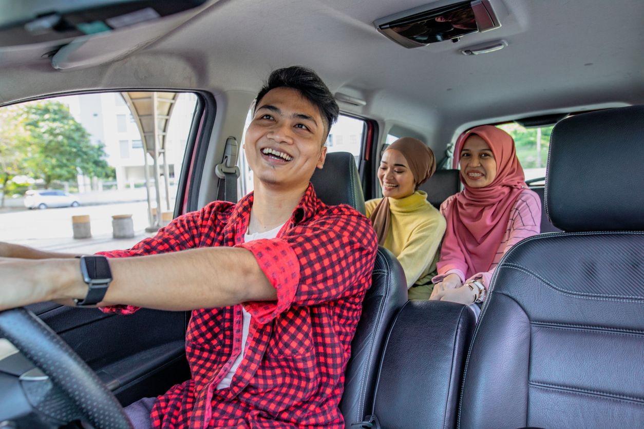 Three friend in the car. The driver is a male and looking to rear seat at mirror and smiling. The passenger is two asian hijab women smiling and laughing in the car