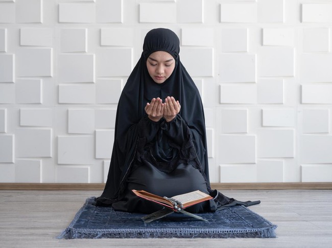 Muslim woman pray on hijab praying with Koran on mat indoors