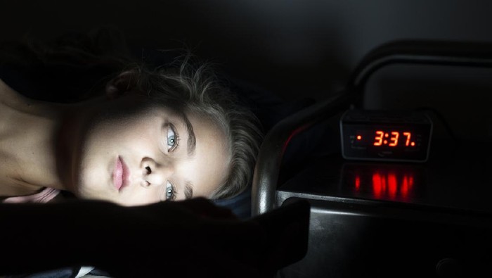 alarm bangun pagi Young teenage girl in bed late at night using her smartphone. Cant sleep or addicted to mobile or social media.