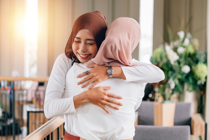 Portrait of young Asian muslim women in happy smile with hijab or head scarf hugs each other indoors. Love and happiness concept