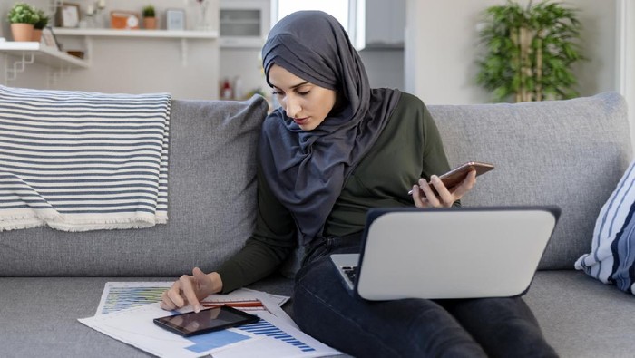 Focused Young Muslim Female Entrepreneur Wearing a Hijab Reading Through Paperwork While Working in Her Home Office. Work Opportunities For Muslim Women Concept. Freelance Concept.
