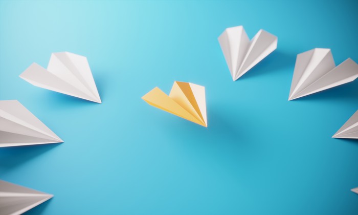 Circle of paper airplanes, and orange colored one standing out from the crowd, can be used leadership/individuality concepts.( 3d render )
