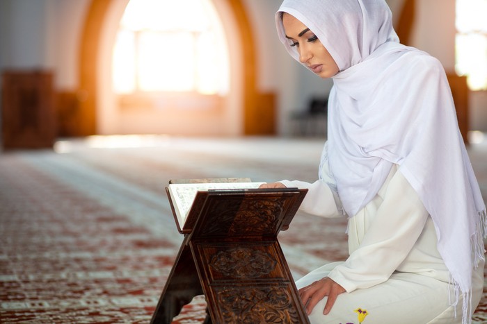 Young Muslim woman praying in mosque with Quran.