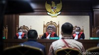 Edhy datang mengenakan kemeja batik berwarna coklat dan mengenakan masker.