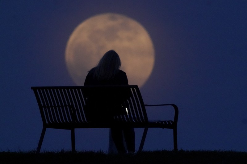 A woman sits at a park as the moon rises, Monday, April 26, 2021, in New Albany, Ind. This moon is a supermoon, meaning it appears larger than an average full moon because it is nearer the closest point of its orbit to Earth. (AP Photo/Charlie Riedel)