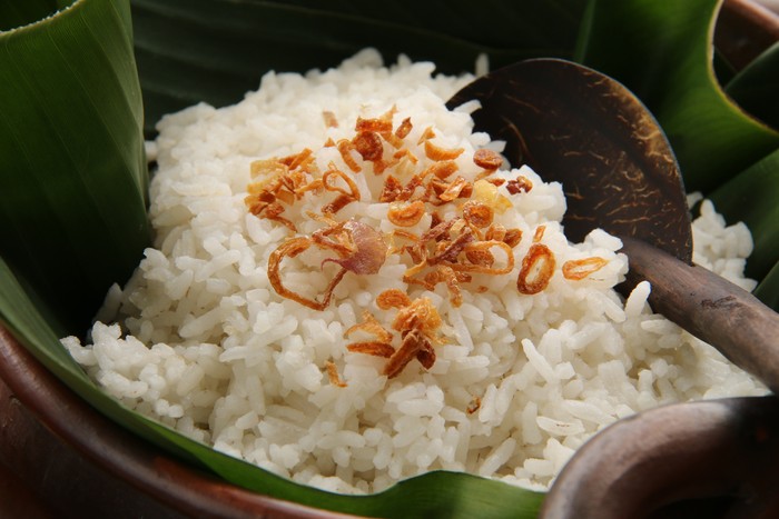 Nasi Uduk, savory rice dish from Betawi, Jakarta. It is steamed mixture of white rice and coconut milk. Commonly sprinkled with some fried shallots. The rice is placed on an earthenware pot lined with banana leaf, which in turn will add some leafy fragrant to the hot rice. A rice ladle made of coconut shell and wood is tucked among the rice grains.