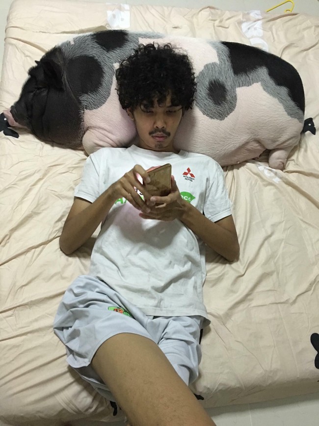 Foto-foto Pattanadon Taesakul tiduran bersama babi yang dihiasi pita pink viral di media sosial. Awalnya orang-orang mengira babi tersebut adalah boneka. Dalam footnya Pattanadon tampak asyik bersandar di badan babi yang super besar itu. Foto: Dok. Facebook Junior the Evil Pig, AFP, thisisprimary