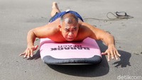 Setelah pemanasan Ajik meletakkan papan seluncur di pasir. Seraya berbaring menghadap papan, Ajik menjelaskan menggerakkan tangannya seperti sedang berenang menggunakan gaya bebas.