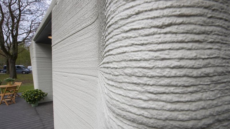 View of the living room with the open kitchen showing the printer layers in the walls of the 3D-printed 94-square meters (1,011-square feet) two-bedroom bungalow resembling a boulder with windows in Eindhoven, Netherlands, Friday, April 30, 2021. The fluid, curving lines of its gray walls look natural. But they are actually at the cutting edge of housing construction in the Netherlands and around the world. They were 3D printed at a nearby factory. (AP Photo/Peter Dejong)