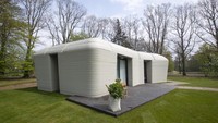 View of the living room with the open kitchen showing the printer layers in the walls of the 3D-printed 94-square meters (1,011-square feet) two-bedroom bungalow resembling a boulder with windows in Eindhoven, Netherlands, Friday, April 30, 2021. The fluid, curving lines of its gray walls look natural. But they are actually at the cutting edge of housing construction in the Netherlands and around the world. They were 3D printed at a nearby factory. (AP Photo/Peter Dejong)
