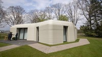 View of the living room with the open kitchen showing the printer layers in the walls of the 3D-printed 94-square meters (1,011-square feet) two-bedroom bungalow resembling a boulder with windows in Eindhoven, Netherlands, Friday, April 30, 2021. The fluid, curving lines of its gray walls look natural. But they are actually at the cutting edge of housing construction in the Netherlands and around the world. They were 3D printed at a nearby factory. (AP Photo/Peter Dejong)