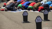 Salat dzuhur berjamaah berlangsung di samping jejeran nisan yang mereka bawa.