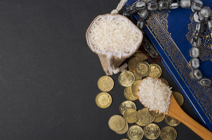 Coins, rosary, Holy Quran and rice in the sack. Zakat concept. Zakat is a form of alm-giving as a religious obligation or tax. Large Arab word right method to read correctly.