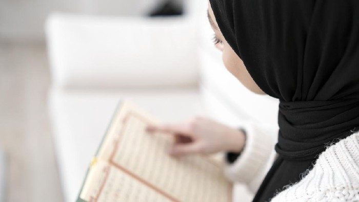 Muslim young woman reading Koran. Horizontal composition.