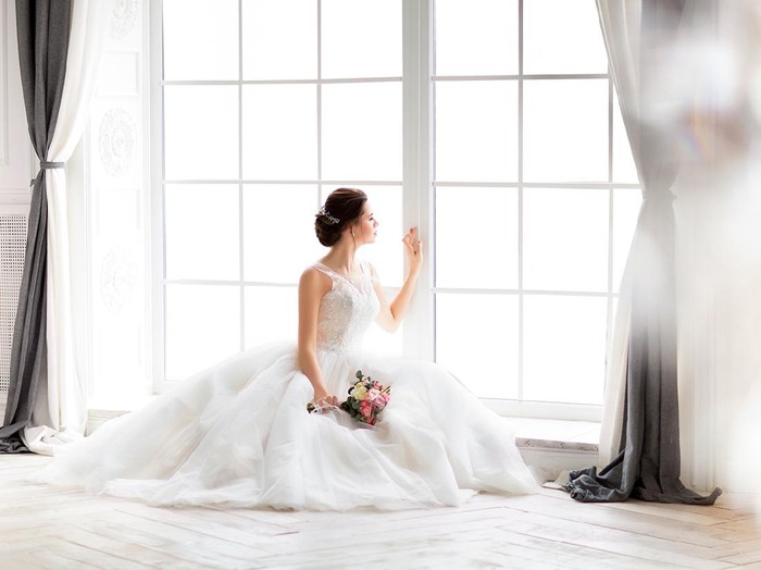 Young beautiful brunette woman with bouquet posing in a wedding dress