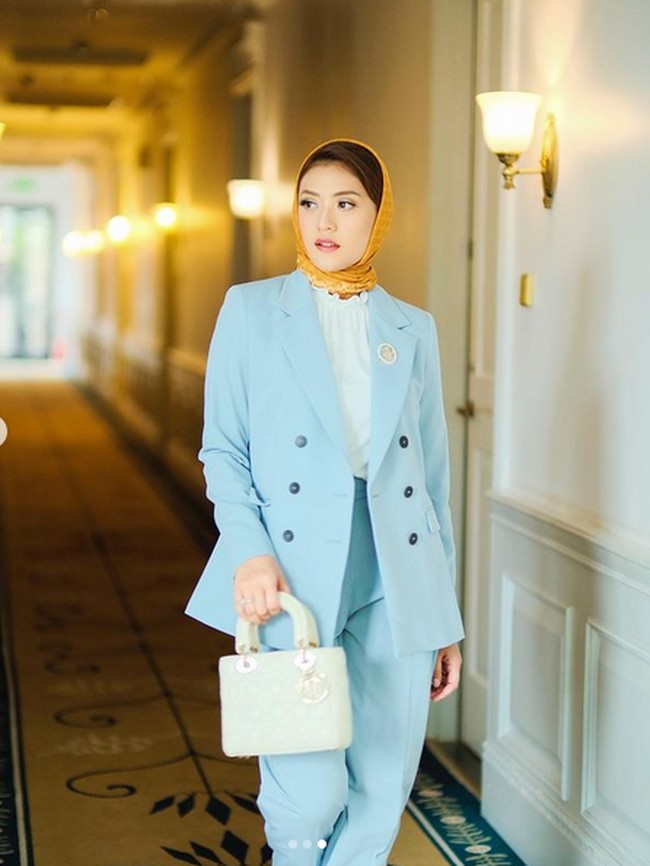 Anissa Aziza tampak elegan dengan gaya monokrom biru muda pada setelan busananya. Kerudung warna oranye yang kontras dengan busana memberi kesan cerah. Foto: Instagram/@anissaaziza, @ayubyayulestariofficial