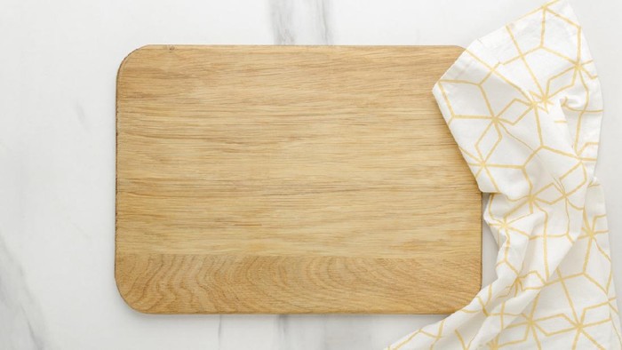 Top view of wooden cutting board, wooden spoons, knife and napkin on the white marble table.Empty space