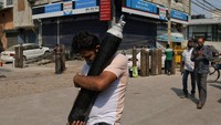 Tampak seorang pria India membawa silinder isi ulang oksigen saat anggota keluarganya tengah mengantri mendapat giliran pasokan oksigen kala berjuang melawan COVID-19.  Foto: AP/Ishant Chauhan