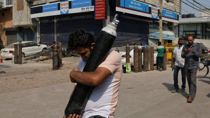 Virus Outbreak FILE - In this May 3, 2021, file photo, a man walks carrying a refilled cylinder as family members of COVID-19 patients wait in queue to refill their oxygen cylinders at Mayapuri area in New Delhi, India. COVID-19 infections and deaths are mounting with alarming speed in India with no end in sight to the crisis. People are dying because of shortages of bottled oxygen and hospital beds or because they couldn’t get a COVID-19 test. (AP Photo/Ishant Chauhan, File)