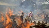 Warga terpaksa melewati rasa panas yang terpancar dari beberapa tumpukan kayu saat kremasi jenazah COVID-19 berlangsung, di sebuah krematorium pinggiran New Delhi, India. Foto: AP/Amit Sharma