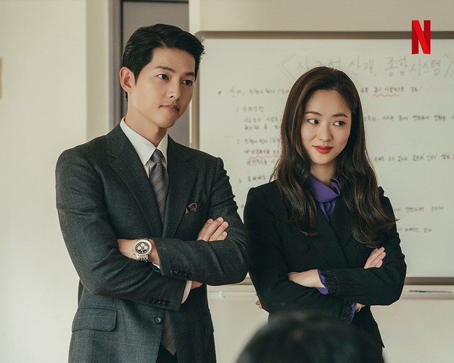 Office look ala Jeon Yeo Bin tak sebatas setelan jas dan celana. Ia juga mengenakan gaun berwarna hitam yang selintas menyerupai coat. Potongan gaun ini mempertegas lekukan tubuh, dengan detail renda di bagian ujung lengan. Foto: dok. tvN