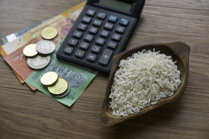 Selective focus of rice, money, coins and calculator on wooden background.
