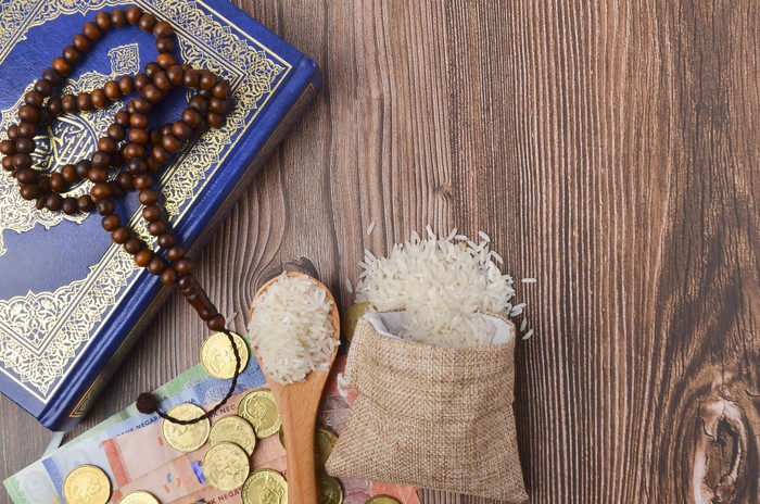 Coins, rosary, Holy Quran and rice in the sack. Zakat concept. Zakat is a form of alm-giving as a religious obligation or tax. Large Arab word right method to read correctly.