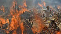 Seorang pria berlari untuk menghindari panas yang dipancarkan dari beberapa tumpukan kayu pemakaman korban COVID-19 di sebuah krematorium di pinggiran New Delhi, India. AP Photo/Amit Sharma  