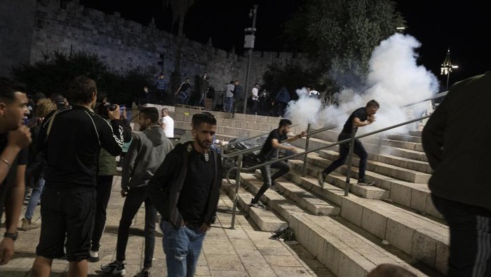 Palestinians react to stun grenades fired by Israeli police to clear the Damascus Gate to the Old City of Jerusalem after clashes at the Al-Aqsa Mosque compound, Friday, May 7, 2021. Palestinian worshippers clashed with Israeli police late Friday at the holy site sacred to Muslims and Jews, in an escalation of weeks of violence in Jerusalem that has reverberated across the region. (AP Photo/Maya Alleruzzo)