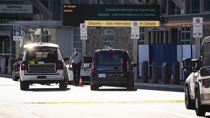 A Royal Canadian Mounted Police officer works at the scene as screens block off an area of the sidewalk after a shooting outside the international departures terminal at Vancouver International Airport, in Richmond, British Columbia, Sunday, May 9, 2021. (Darryl Dyck/The Canadian Press via AP)