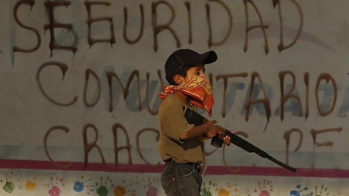Kala Anak-anak Meksiko Angkat Senjata Lawan Kartel Narkoba Community policeman Silvano Martinez guards his 11-year-old nephew Geovanni Martinez as he observes his goats in a pasture outside Ayahualtempa, a town in Guerrero state where residents provide security from the violence of rivaling gangs in Mexico, Wednesday, April 28, 2021. The 11-year-old said he yearns to return to school, closed for the past year by the pandemic, and when asked if he would shoot at an enemy he issued a convincing