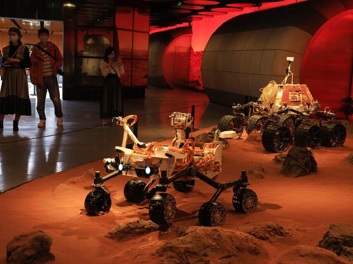 Visitors pass by an exhibition depicting rovers on Mars in Beijing on Friday, May 14, 2021. China says its Mars probe and accompanying rover are to land on the red planet sometime between early Saturday morning and Wednesday Beijing time. (AP Photo/Ng Han Guan)