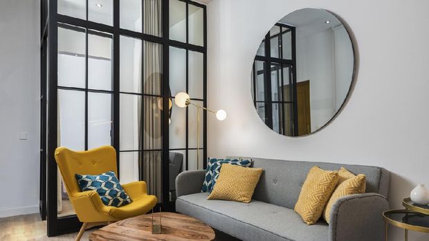 Colorful and cozy living room with a designer armchair and sofa along with a round decorative mirror and glass wall.