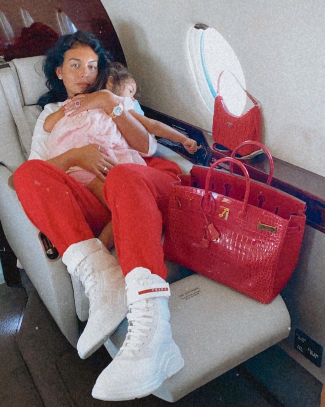 Berikut potret kebersamaan Georgina Rodriguez bersama anaknya saat naik private jet. Kali ini wanita yang disebut sebagai salah satu selebgram berbayar termahal di kalangan para WAGs itu tampak membawa tas Hermes merah andalannya. Foto: Instagram @georginagio