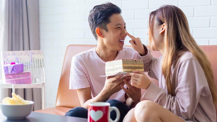 playful young asian couple celebrating Anniversary together at home, playing with the cake