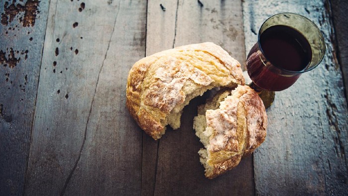 A rustic high contrast still life of bread and wine, representing the Last Supper of Jesus Christ, his blood and body.  The elements rest on a weathered gray wood background.  Vertical with copy space.