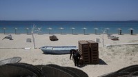 Pekerja mengatur kursi berjemur saat yang lain memasang payung di pantai Plaka di pulau Aegean Naxos, Yunani. AP Photo/Thanassis Stavrakis  