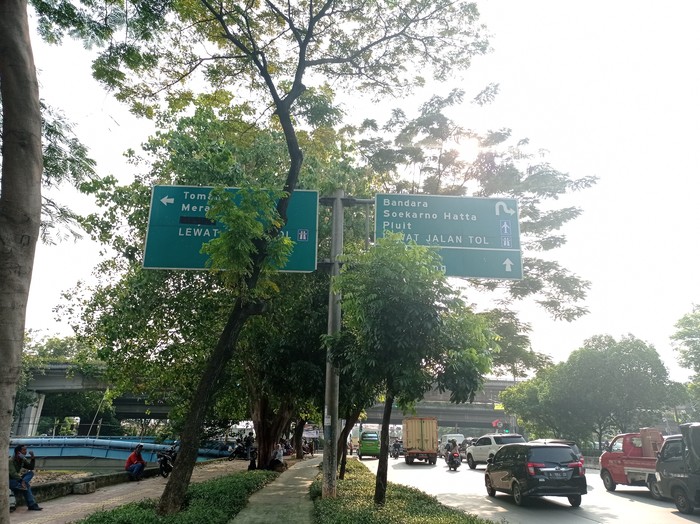 Petunjuk arah tol di Jalan Daan Mogot terhalang pohon dan berada di atas trotoar.