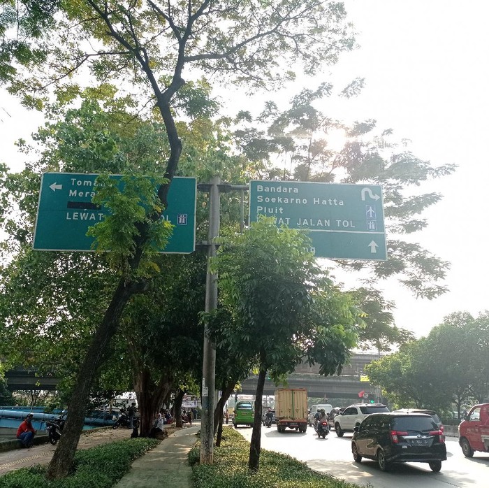 Petunjuk arah tol di Jalan Daan Mogot terhalang pohon dan berada di atas trotoar.