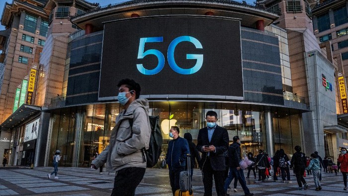 BEIJING, CHINA - April 16: Orang-orang berdiri di depan toko Apple yang mengiklankan ponsel berkemampuan 5G pada 16 April 2021 di sebuah distrik perbelanjaan di Beijing, Cina. China mengumumkan pertumbuhan ekonomi yang kuat sebesar 18,3 persen pada kuartal pertama 2021, dibandingkan dengan periode yang sama tahun lalu ketika ekonomi terbesar kedua di dunia itu terhenti karena pandemi COVID-19. (Photo by Kevin Frayer/Getty Images)