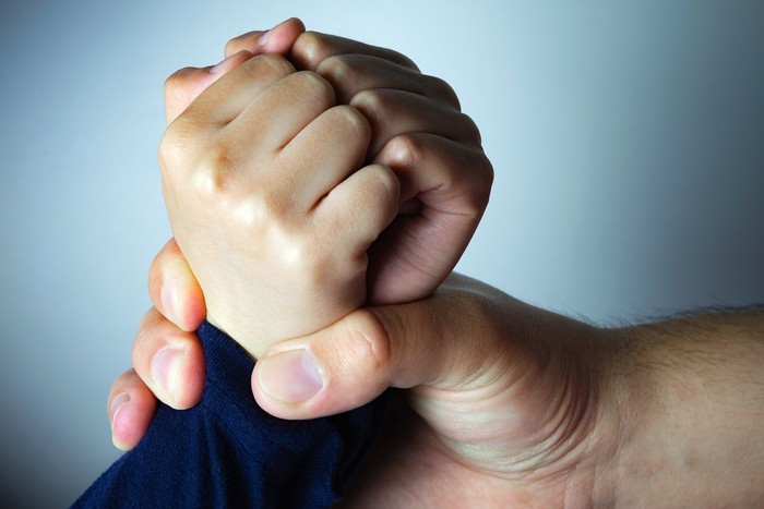 Father roughly holds the hands of his son. Child abuse, domestic violence. Concept image.