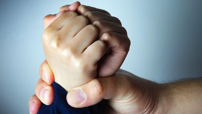 Father roughly holds the hands of his son. Child abuse, domestic violence. Concept image.