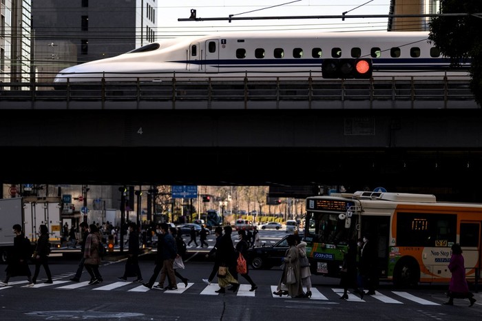 People cross a street while a shinkansen, or high speed bullet train, arrives in Tokyo on February 6, 2021. (Photo by Charly TRIBALLEAU / AFP)