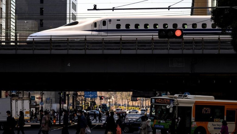 People cross a street while a shinkansen, or high speed bullet train, arrives in Tokyo on February 6, 2021. (Photo by Charly TRIBALLEAU / AFP)