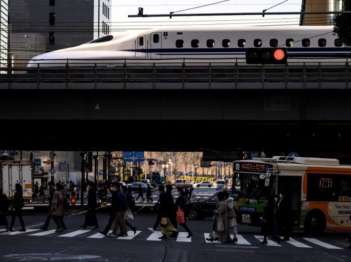People cross a street while a shinkansen, or high speed bullet train, arrives in Tokyo on February 6, 2021. (Photo by Charly TRIBALLEAU / AFP)